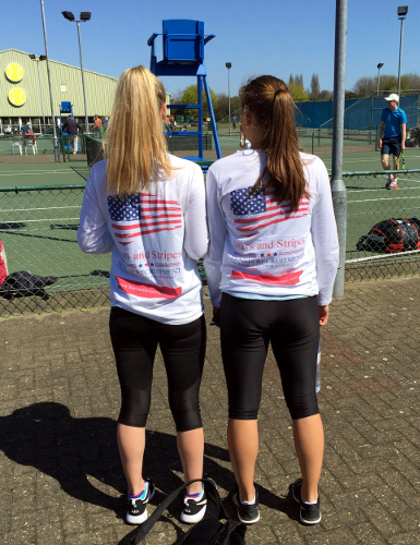 Two female tennis players wearing Stars and Stripes Tennis Recruitment tops, seen from behind